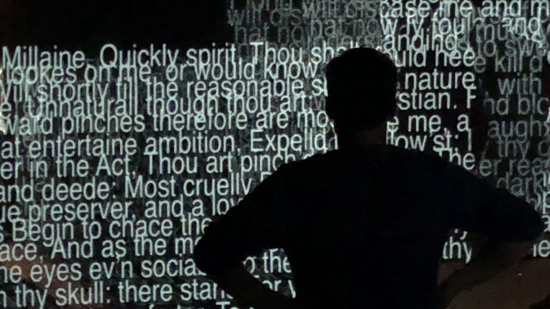 A silhouette of a man standing in front of a wall of projected captions